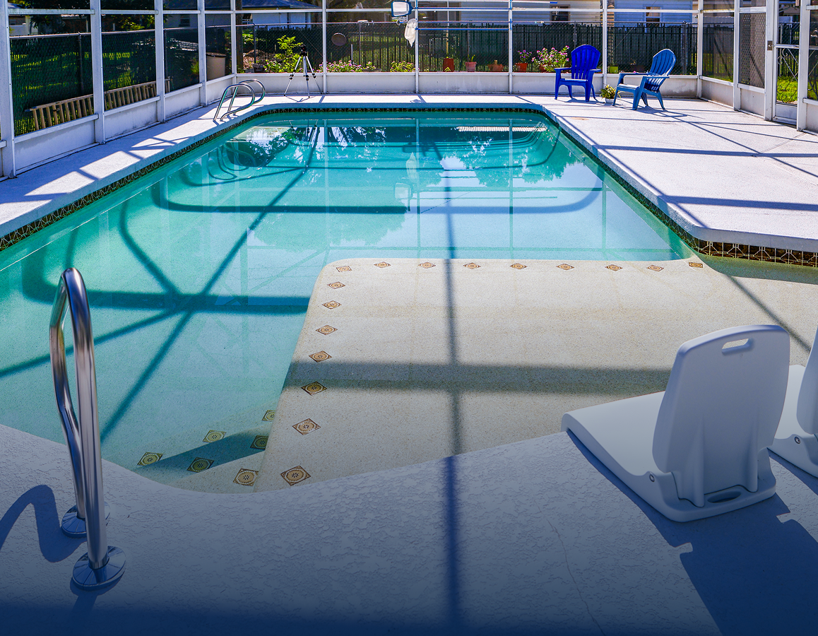 Outdoor swimming pool with clear blue water, metal handrails, and a white deck chair on a sunlit patio