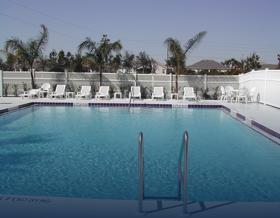 Outdoor swimming pool with blue water, white lounge chairs, and palm trees under a clear sky