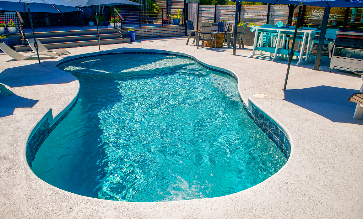 Curved turquoise swimming pool with white deck and lounge chairs in a sunny outdoor patio area