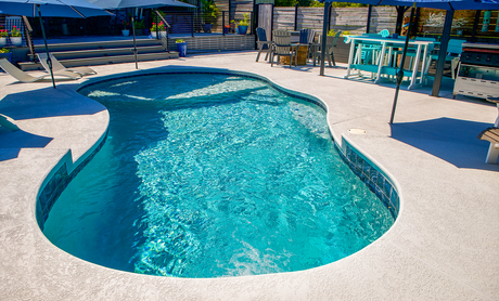Curved turquoise swimming pool with white deck and lounge chairs in a sunny outdoor patio area