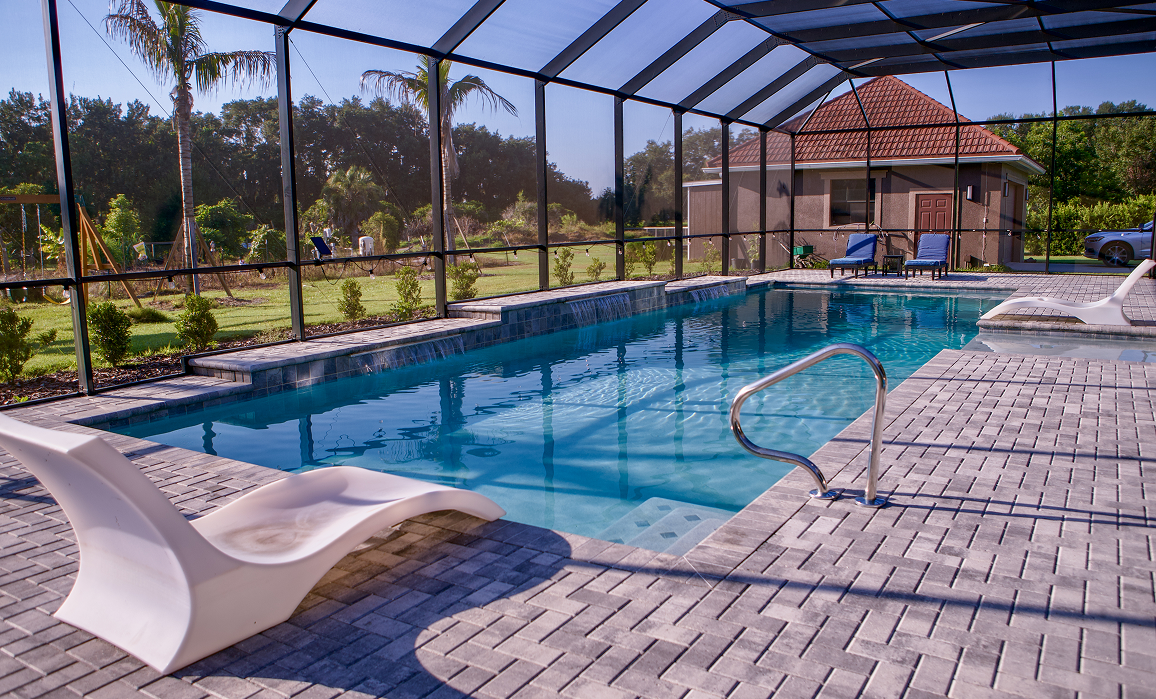 Outdoor screened swimming pool with blue water, lounge chairs, and a patio under sunny skies
