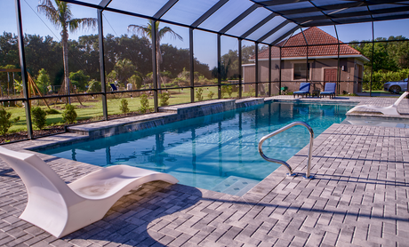 Outdoor screened swimming pool with blue water, lounge chairs, and a patio under sunny skies