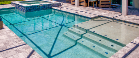 Covered backyard swimming pool with a safety net over blue water and stone patio tiles