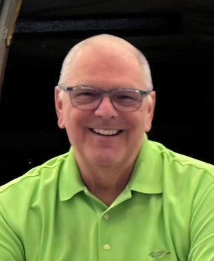 Smiling person in glasses wearing a bright green polo shirt against a dark background