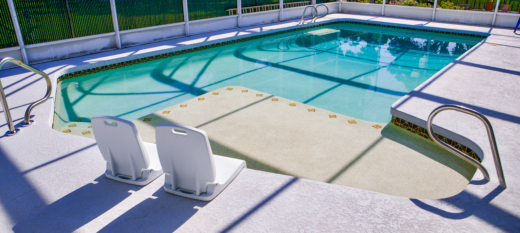 Backyard swimming pool with a safety cover, white lounge chairs, and green fencing around it