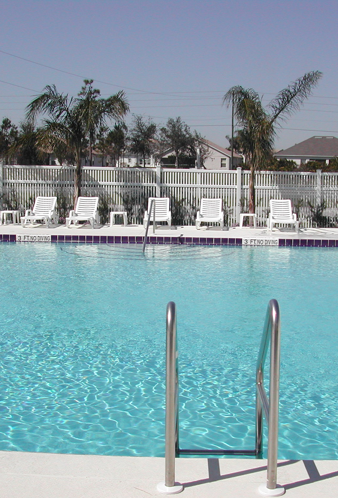 Swimming pool with ladder, blue water, and white lounge chairs along the far side.