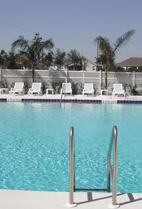 Swimming pool with ladder, blue water, and white lounge chairs along the far side.