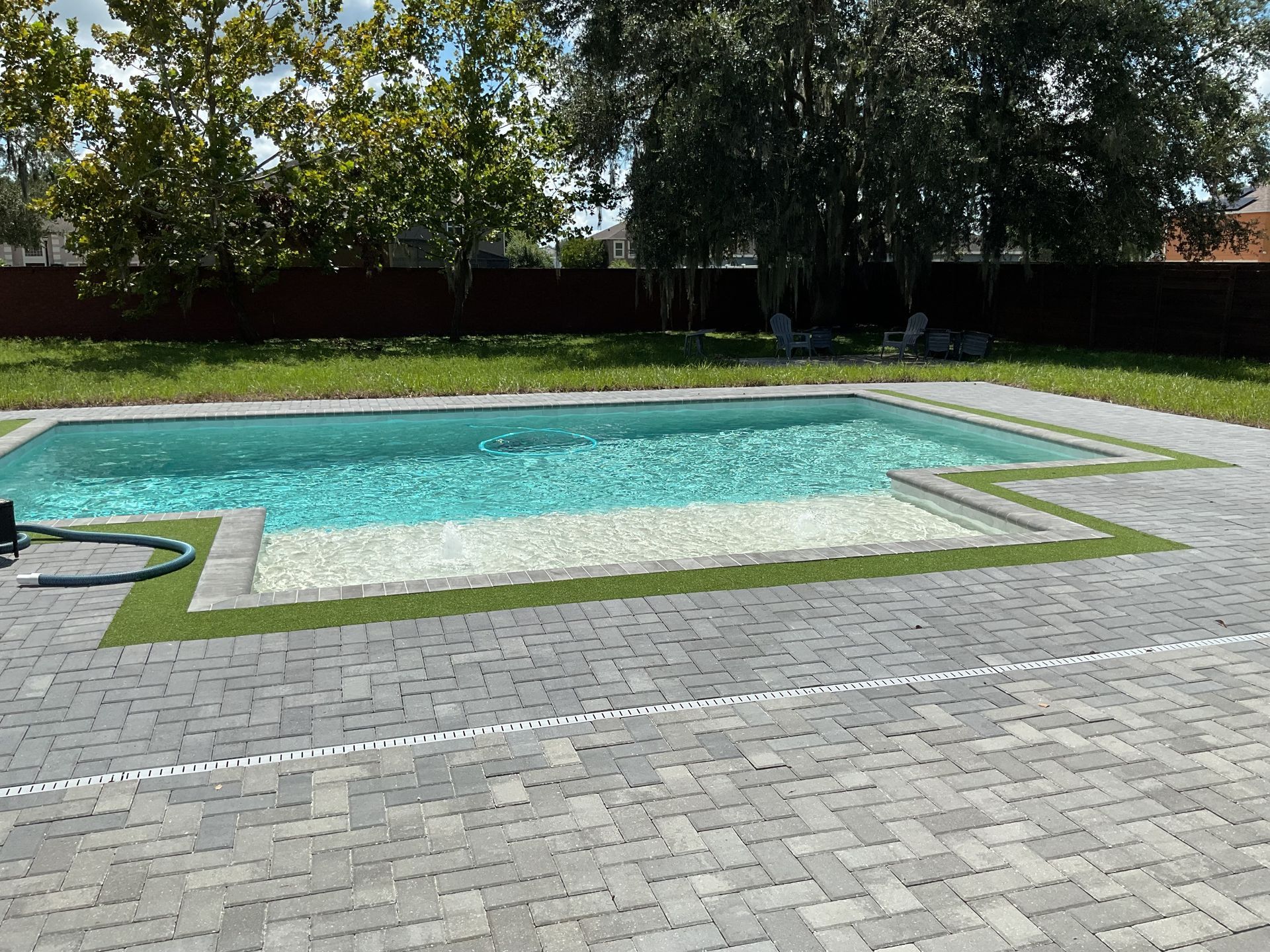 Backyard swimming pool with turquoise water, stone patio, and trees along the fence line