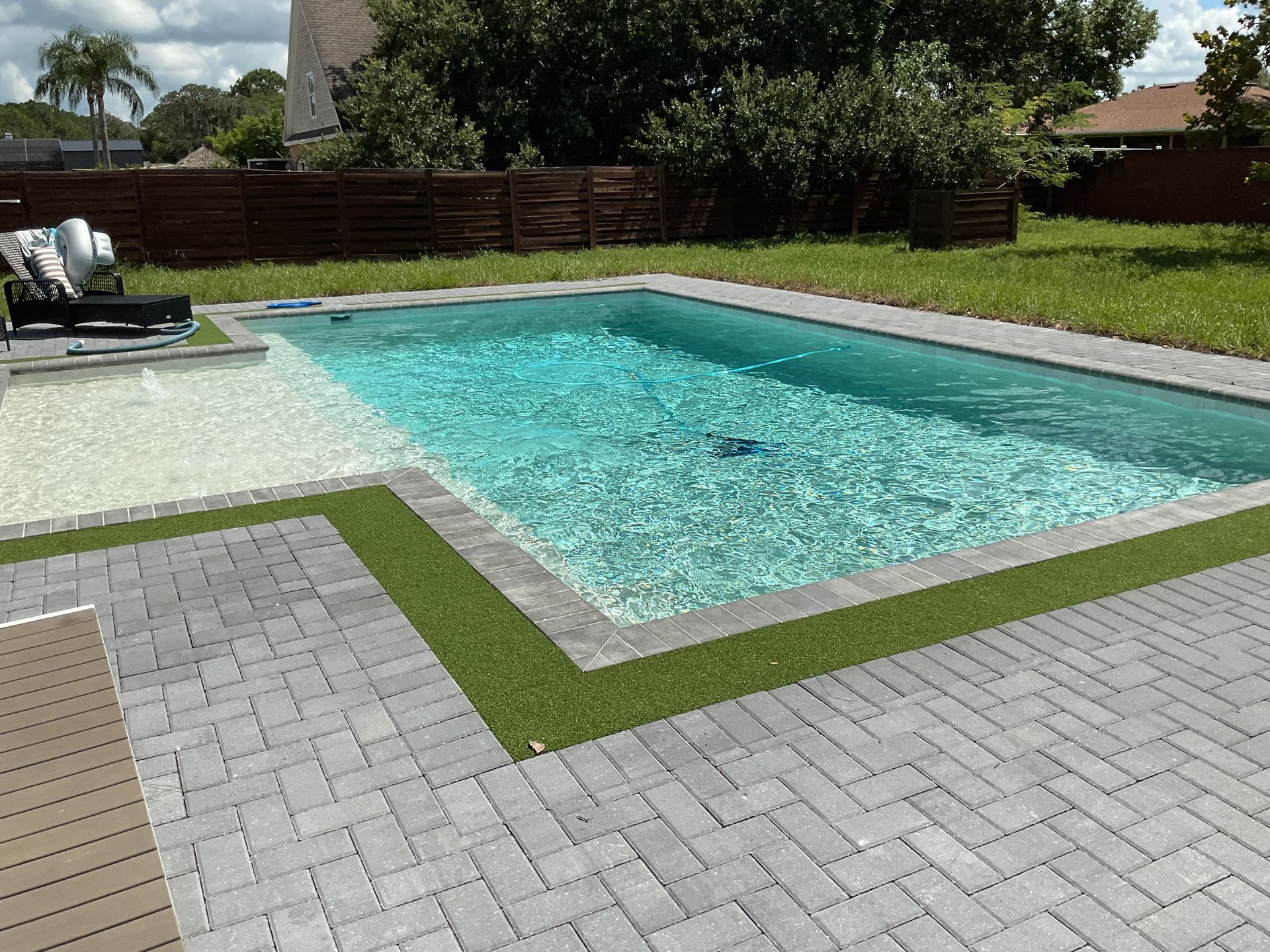 Backyard swimming pool with turquoise water, stone patio, and lawn under bright sunlight