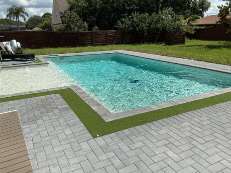 Backyard swimming pool with turquoise water, stone patio, and lawn under bright sunlight