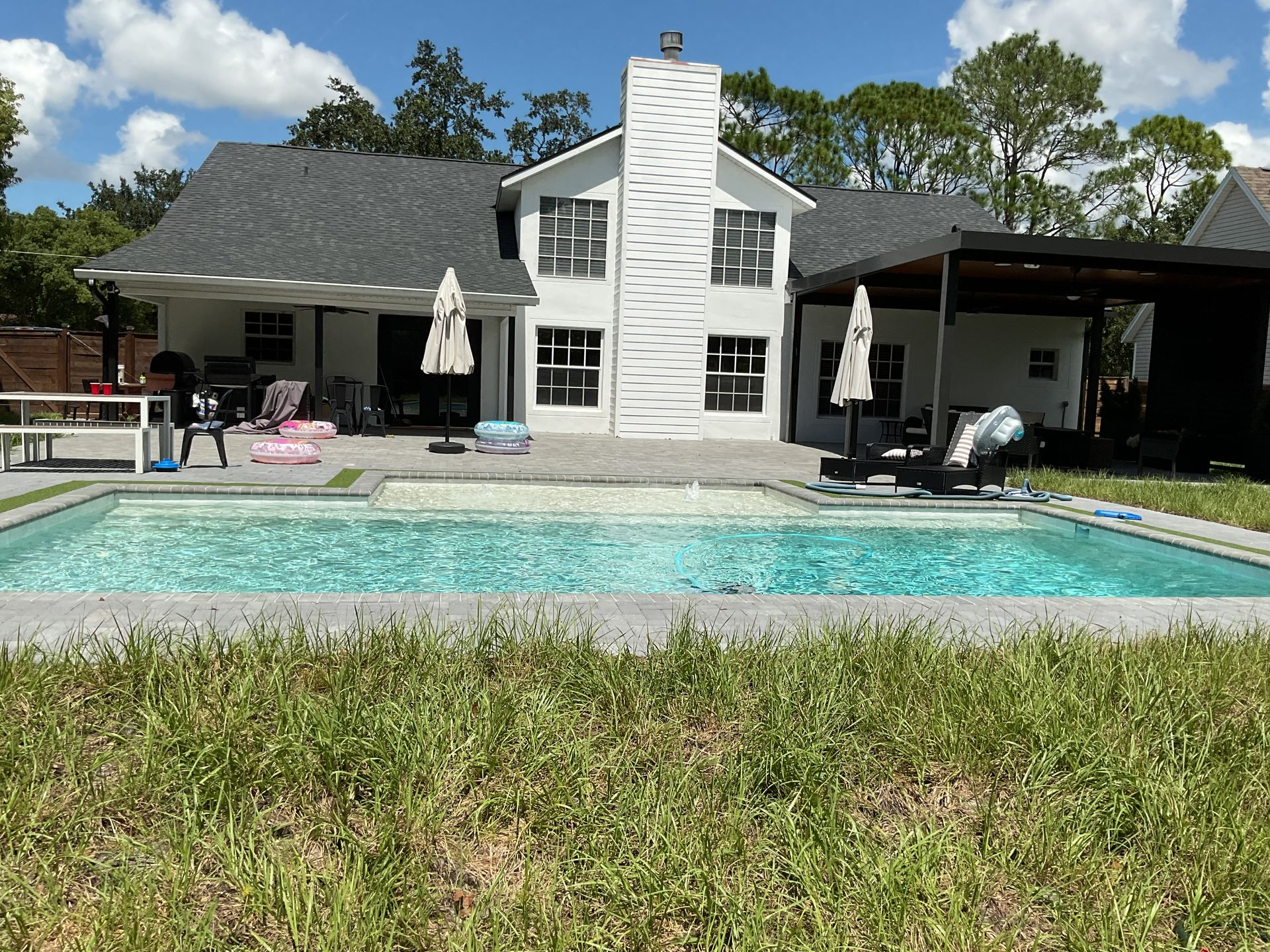 Modern house with a swimming pool, lounge chairs, and a lawn under a blue sky