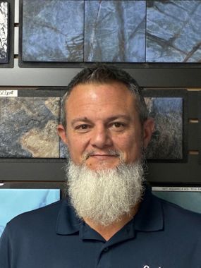 Man smiling in front of framed stone tile samples on a wall