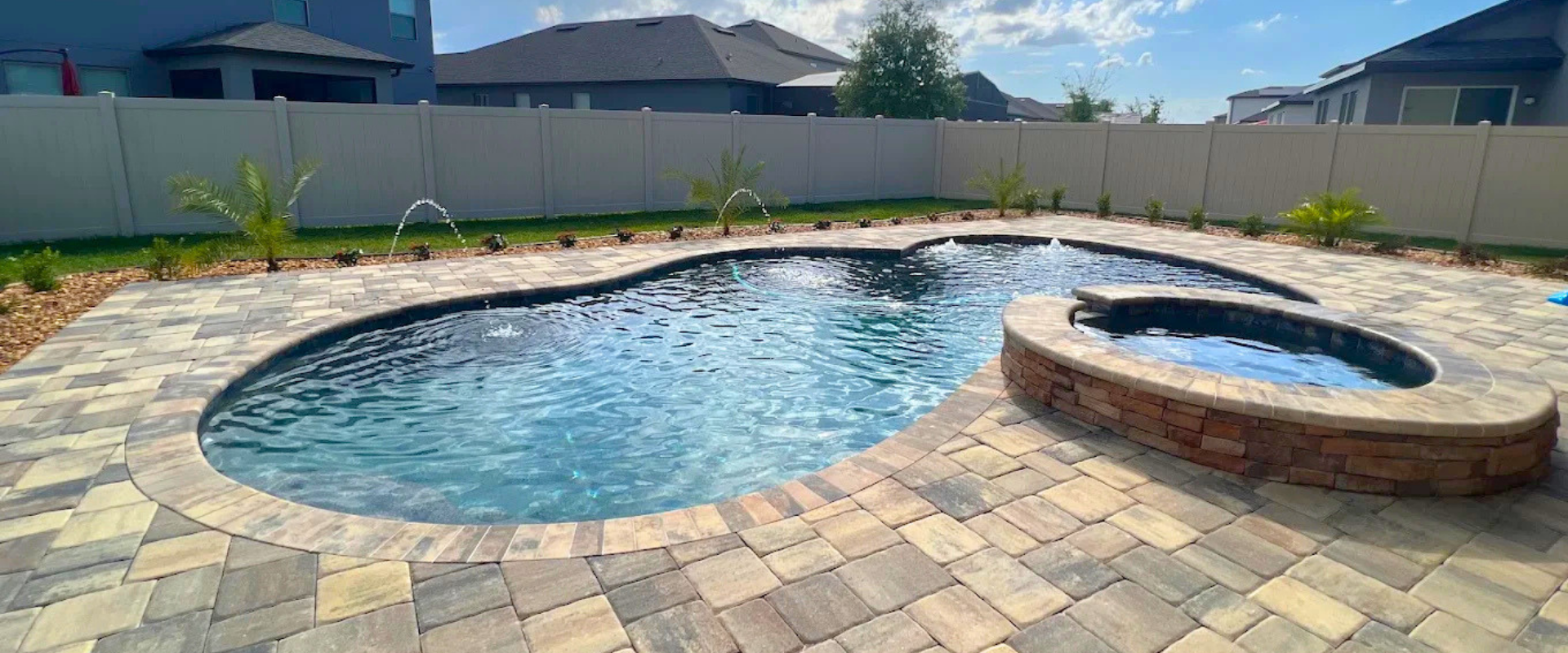 Backyard pool with a stone patio and raised spa under a bright blue sky