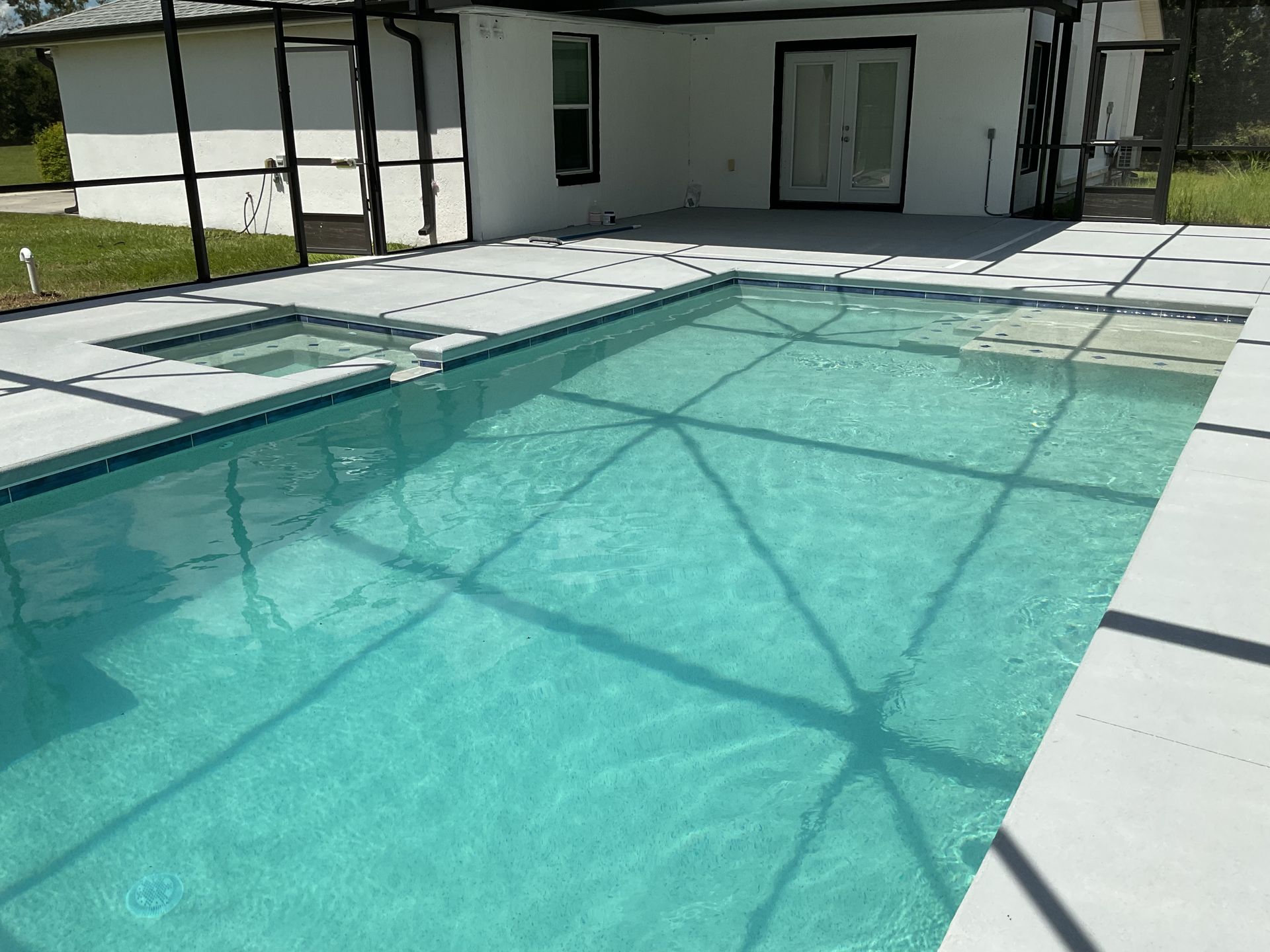 Backyard swimming pool with turquoise water beside a white house and patio area
