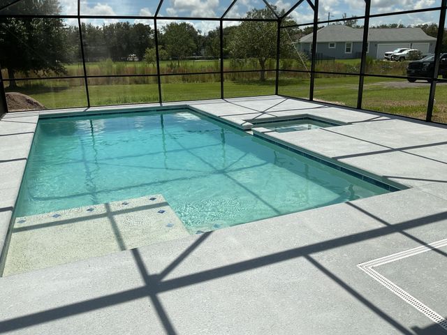 Screened backyard pool with turquoise water, white deck, and grassy field beyond.