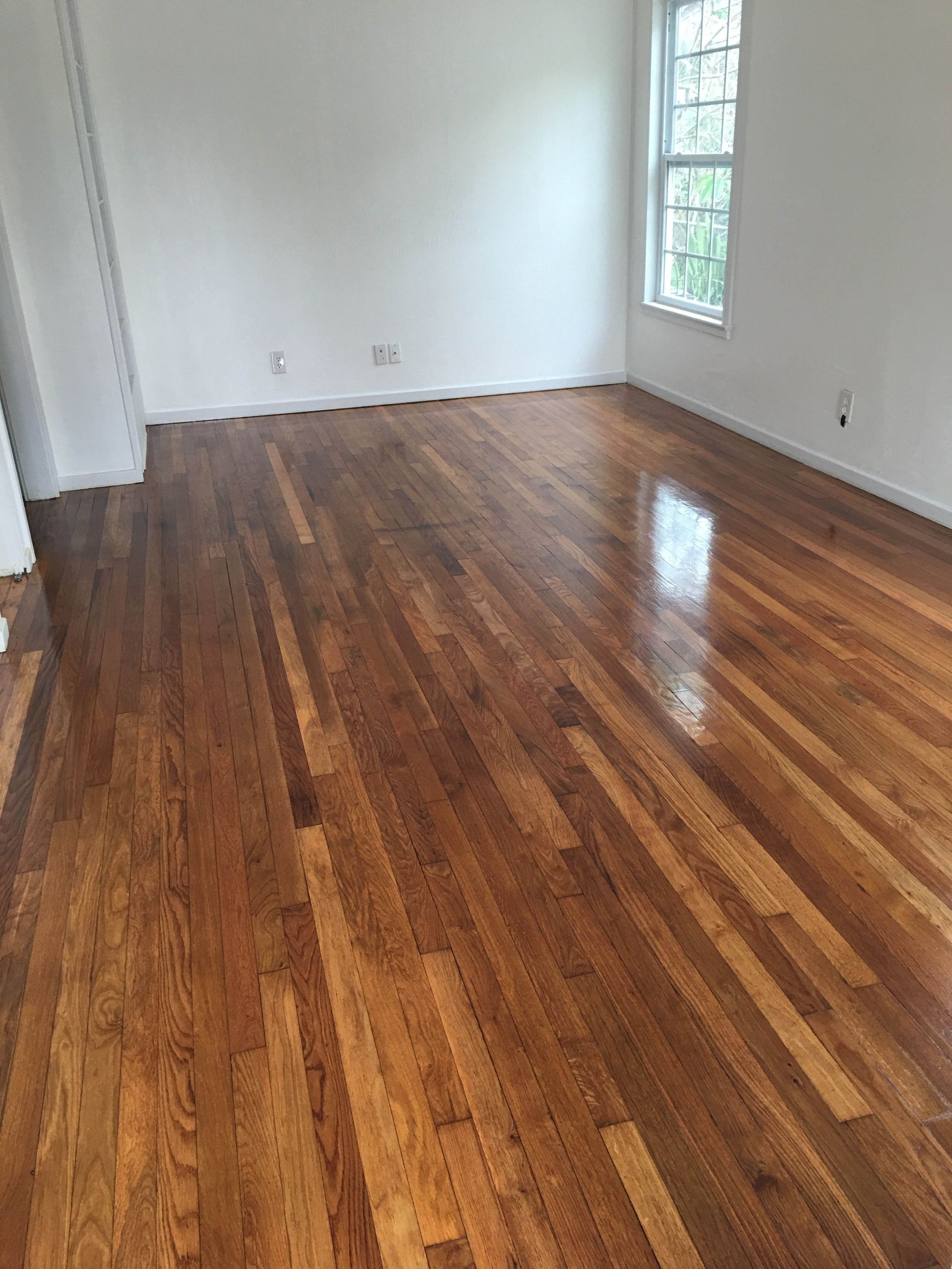 Empty room with glossy hardwood floors, white walls, and a window on the right.