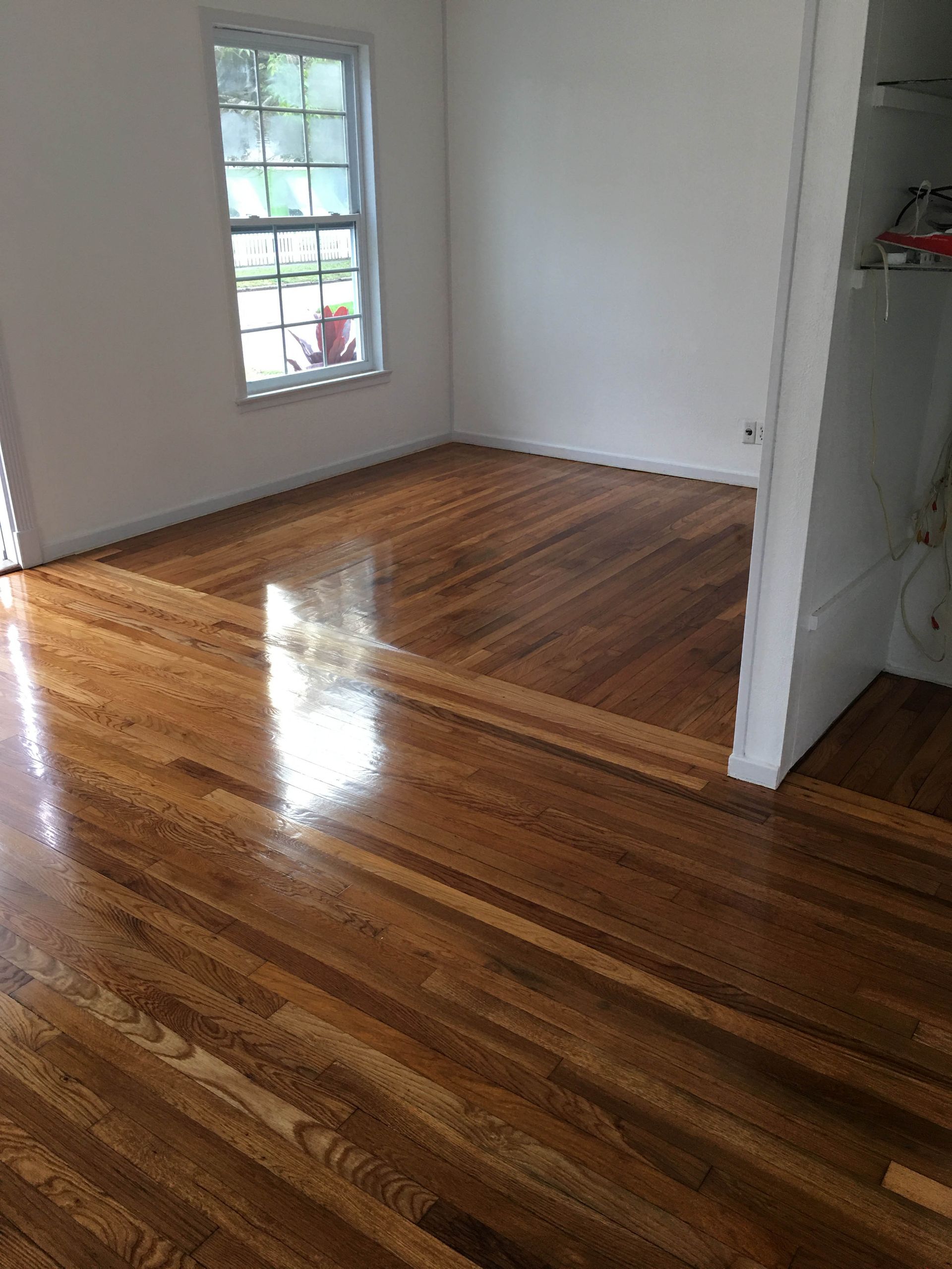 Empty room with glossy hardwood floors, white walls, and a window letting in daylight