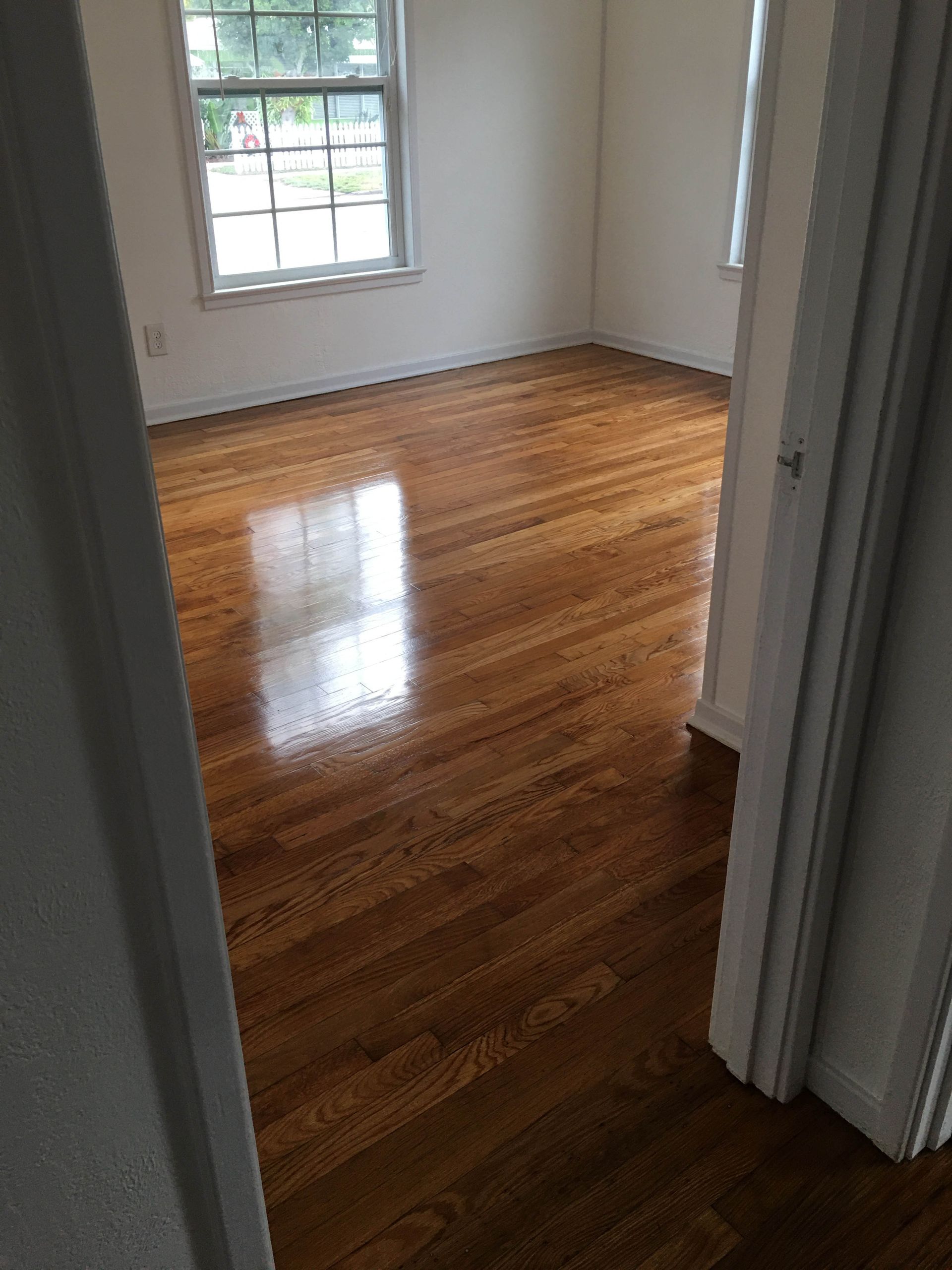Empty room with polished hardwood floors and a window letting in daylight