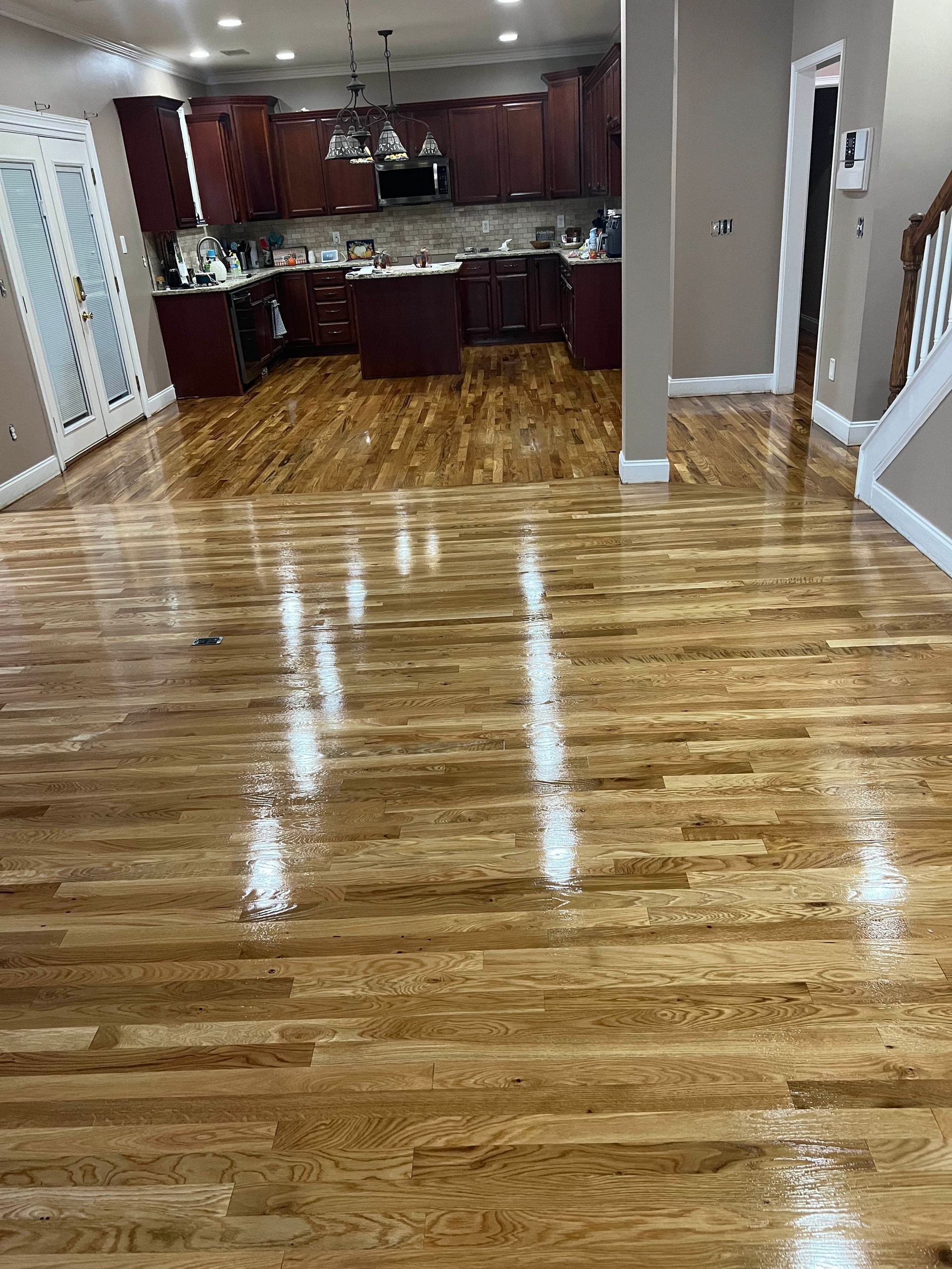 Empty hardwood-floored kitchen and dining area with red cabinets and bright overhead lights
