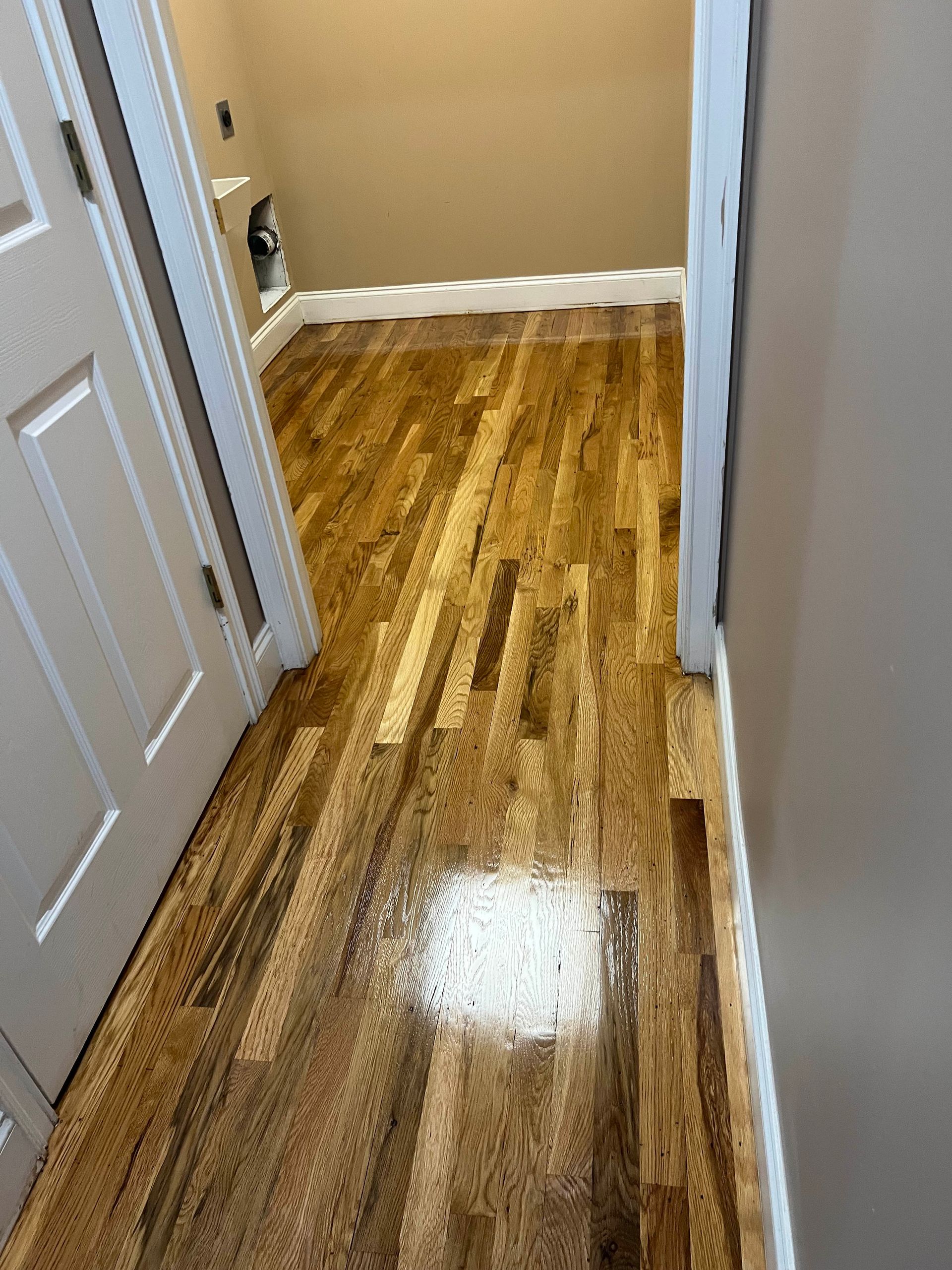 Shiny hardwood hallway floor with white doors and beige walls, leading to a small room.