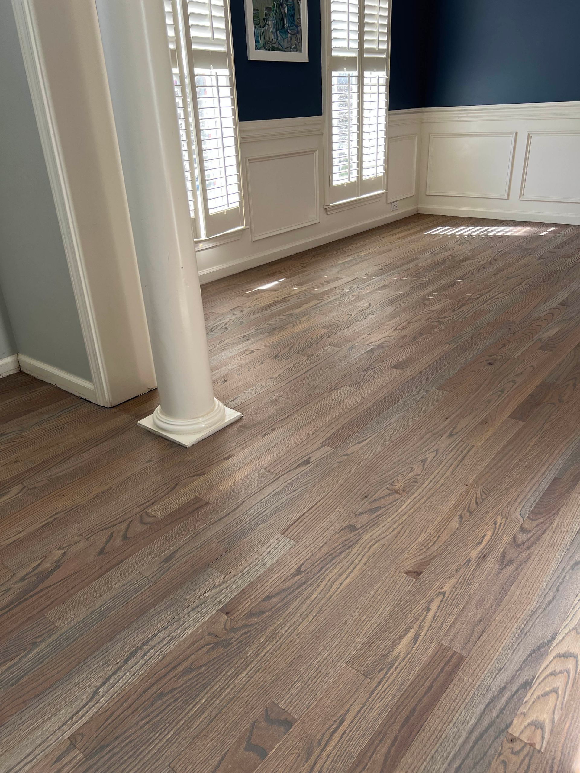 Empty living room with wood-look flooring, white columns, and French doors with shutters
