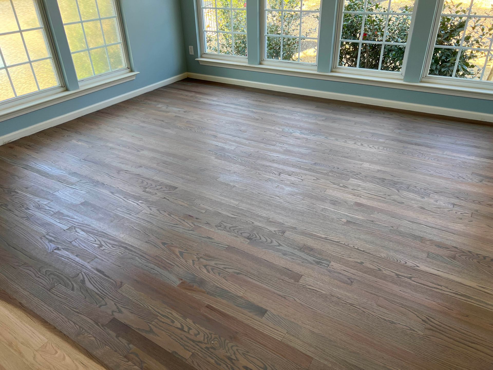 Empty room with wide wood flooring and large windows letting in natural light