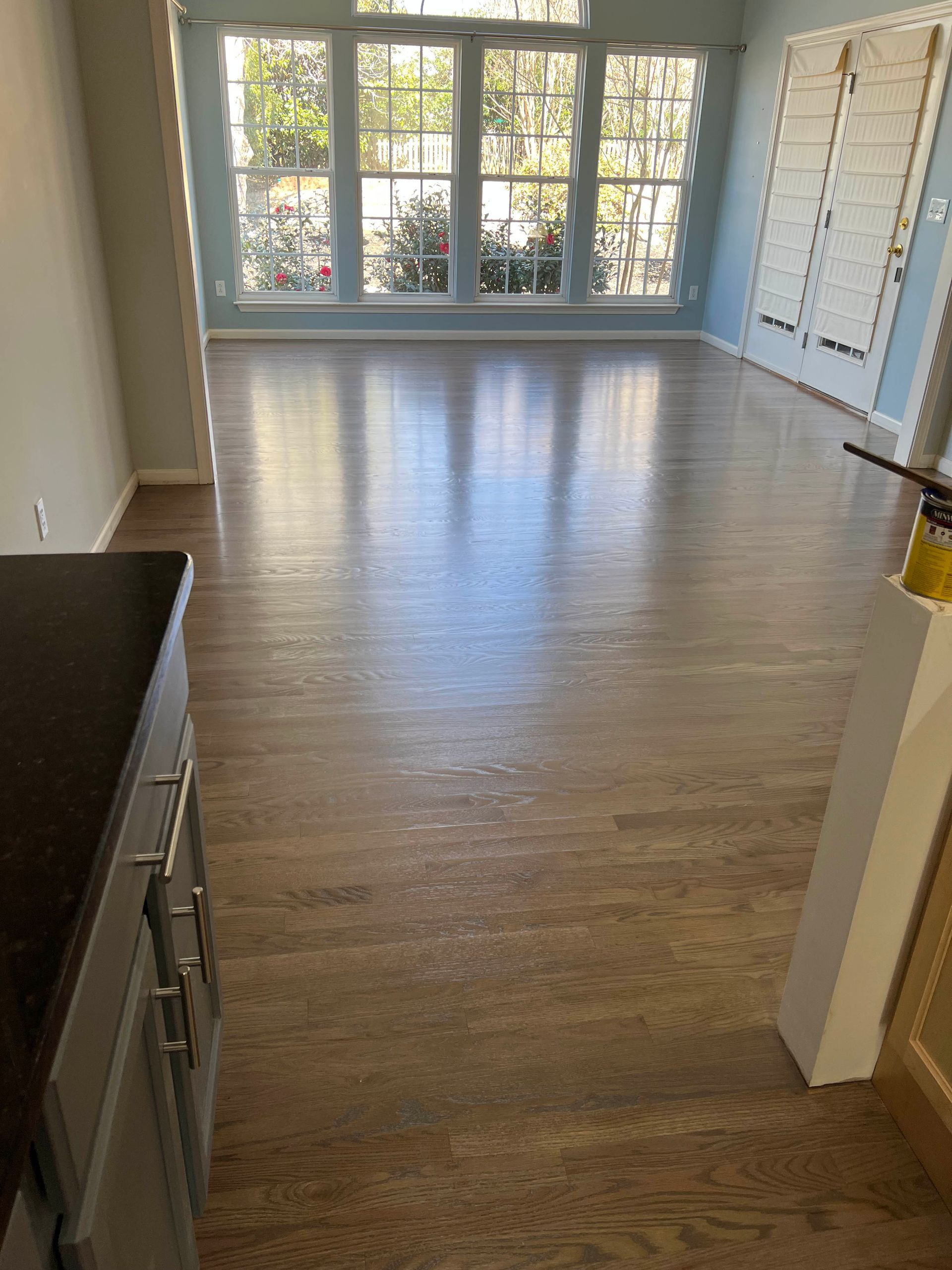 Empty bright room with hardwood floors and large windows with white trim
