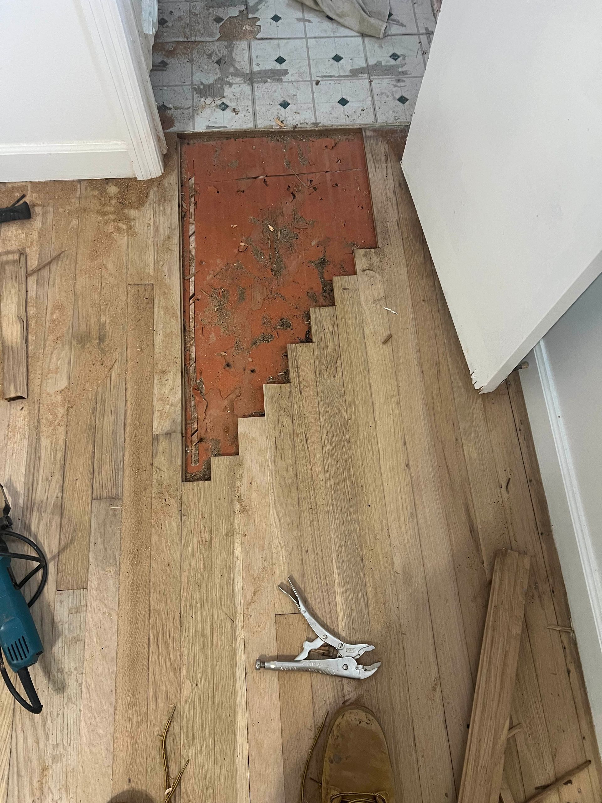 Damaged floor with missing wood flooring and a red patch near a doorway, with a small broken white object on the floor