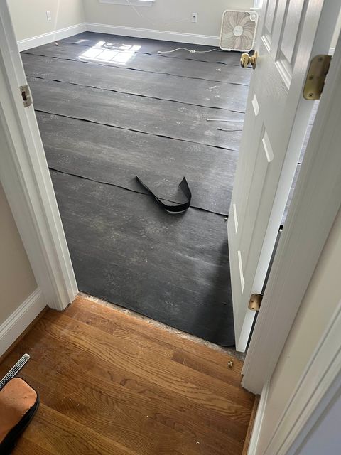 Hallway view into a room with gray floor underlayment and a black strap on the floor.