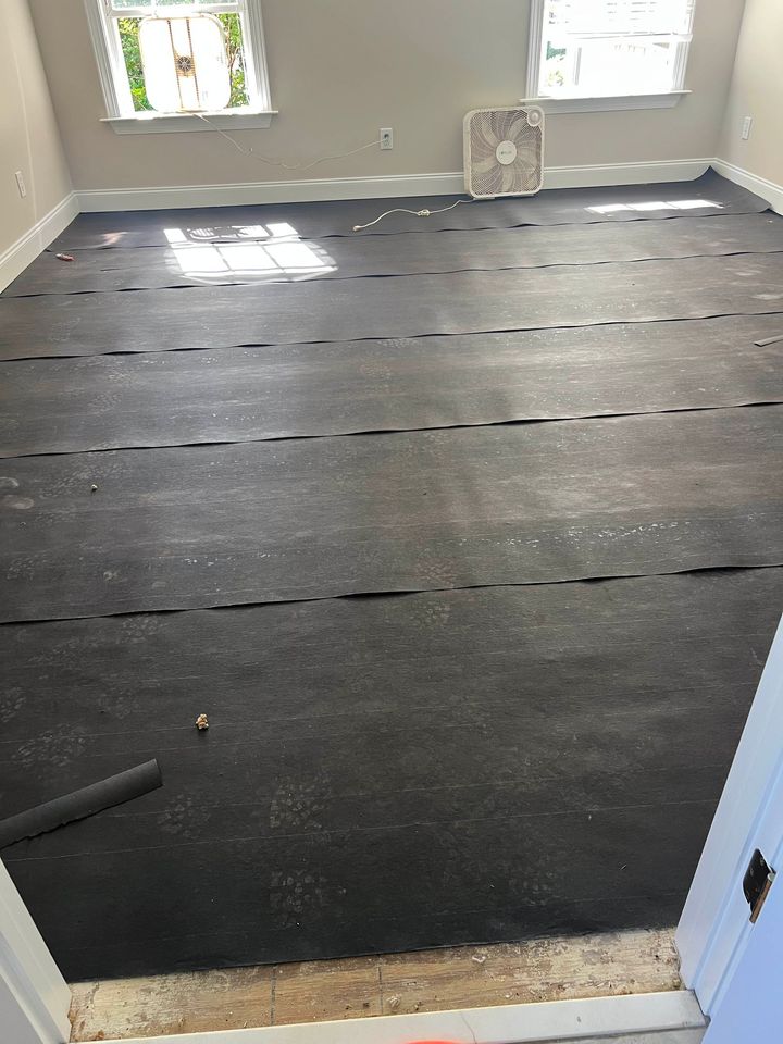 Bare room with dark carpet laid over subfloor, windows at the far wall, and a doorway in the foreground