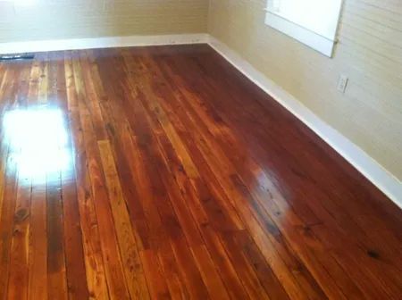 Empty room with glossy hardwood floors, beige walls, and a window letting in bright light