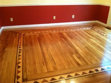 Empty room with polished hardwood floor, red walls, and white baseboards and trim.