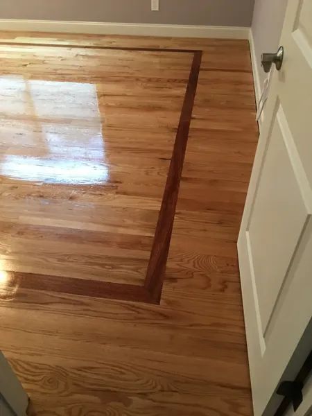 Wooden hardwood floor with a raised rectangular panel or hatch near a white door
