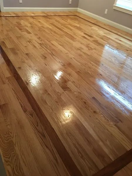 Polished hardwood floor in an empty room with white baseboards and gray walls