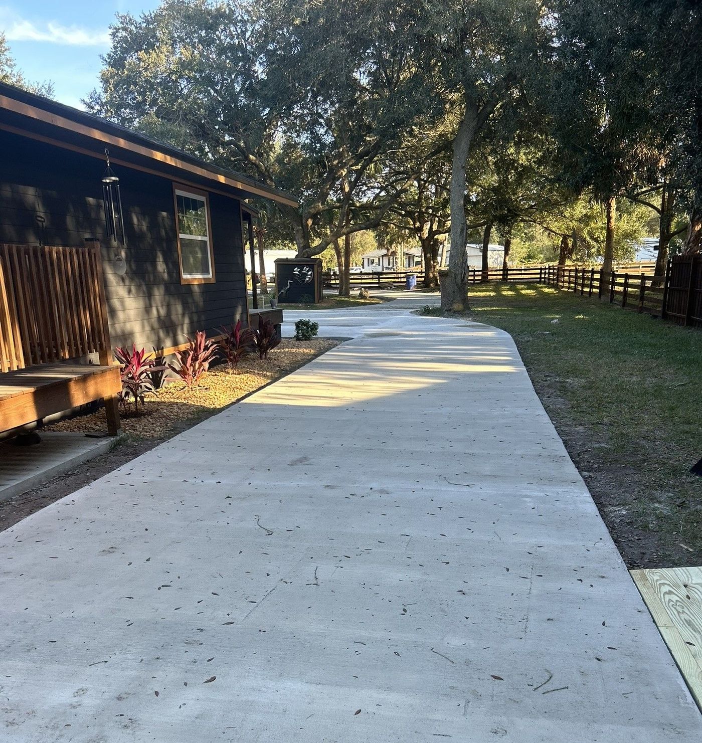 Concrete walkway beside a wooden building, shaded by trees in a park-like outdoor setting