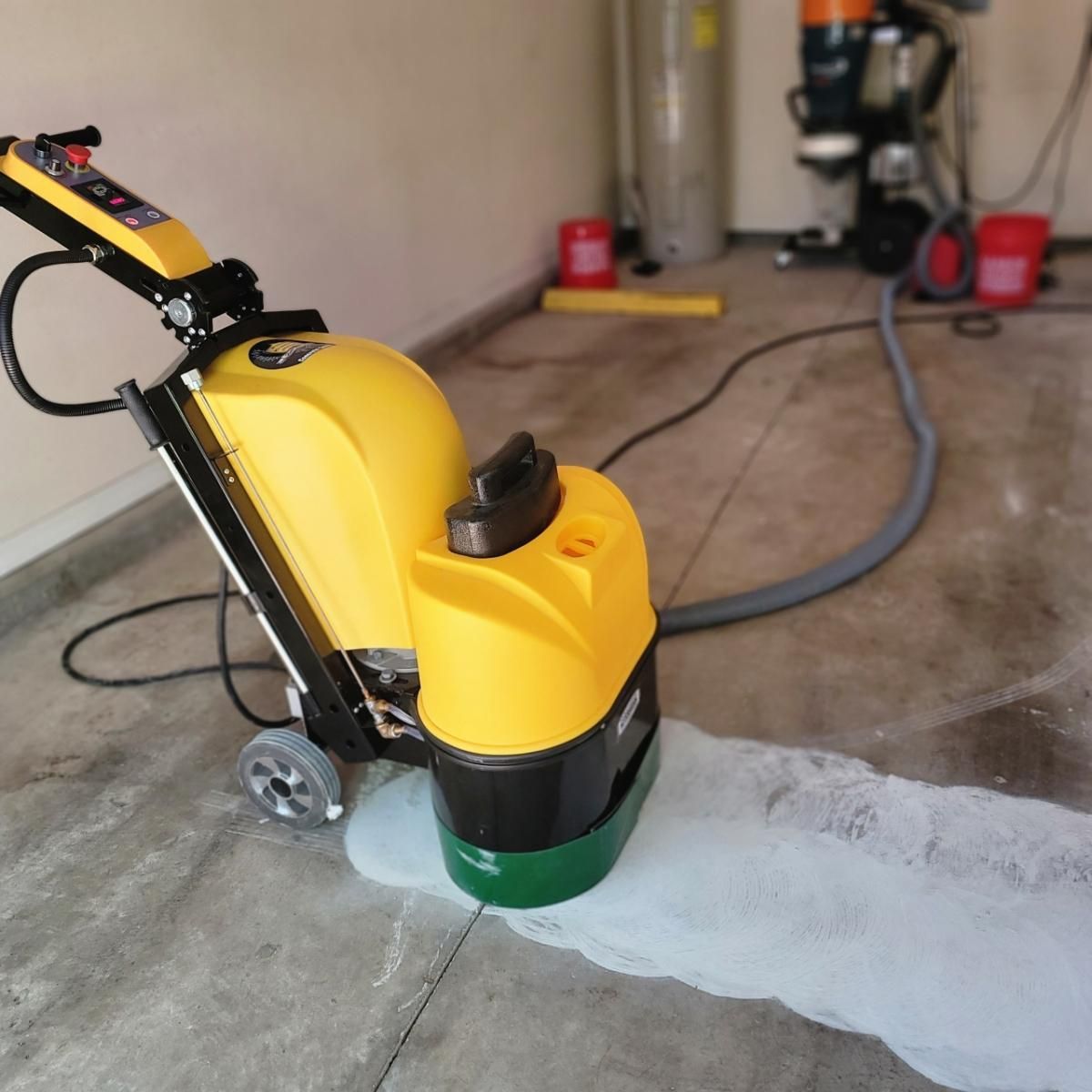 Yellow floor scrubber cleaning a soapy concrete garage floor.
