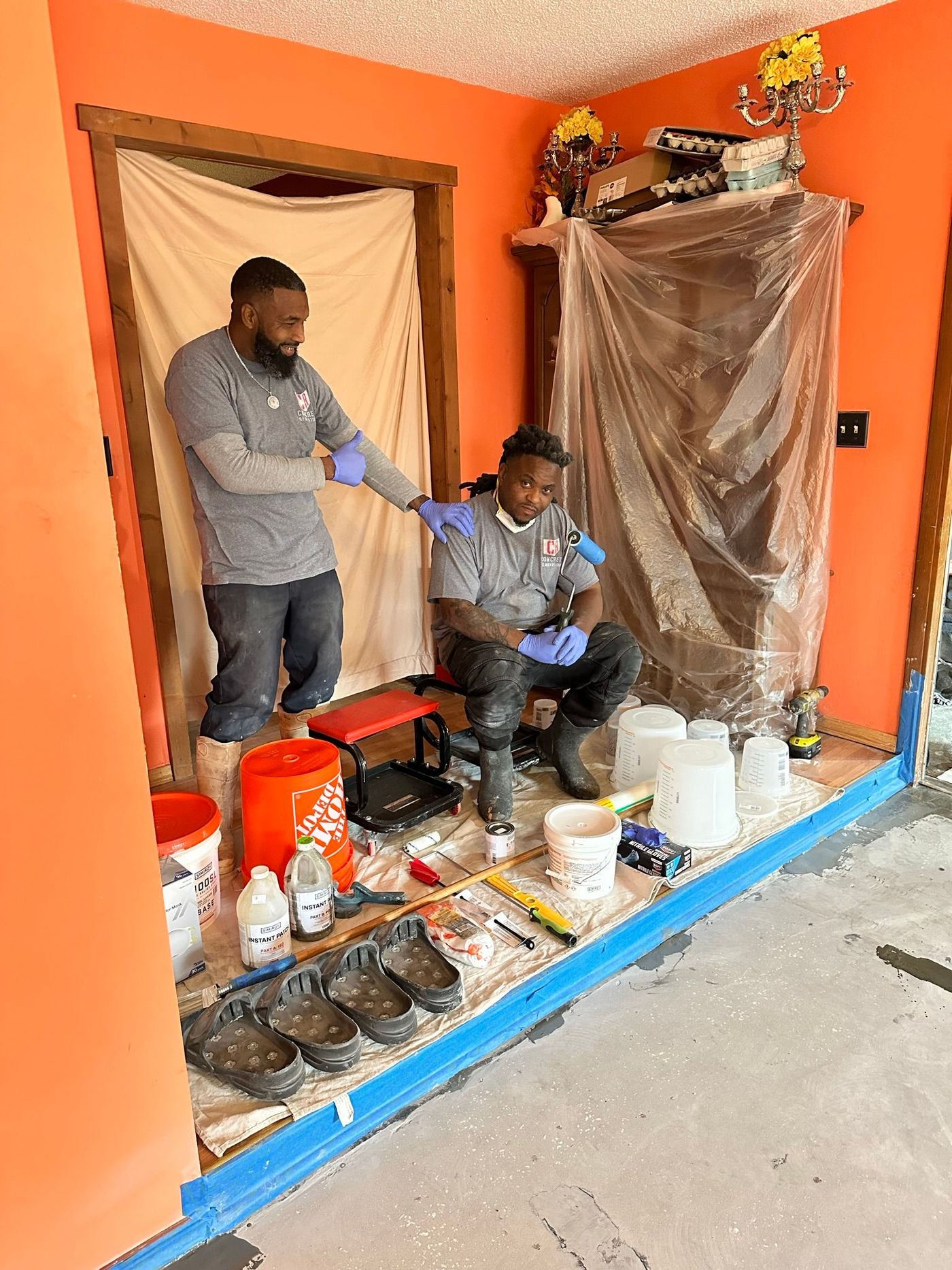 Two people at an epoxy mixing station, handling cups and containers beside a covered display case.