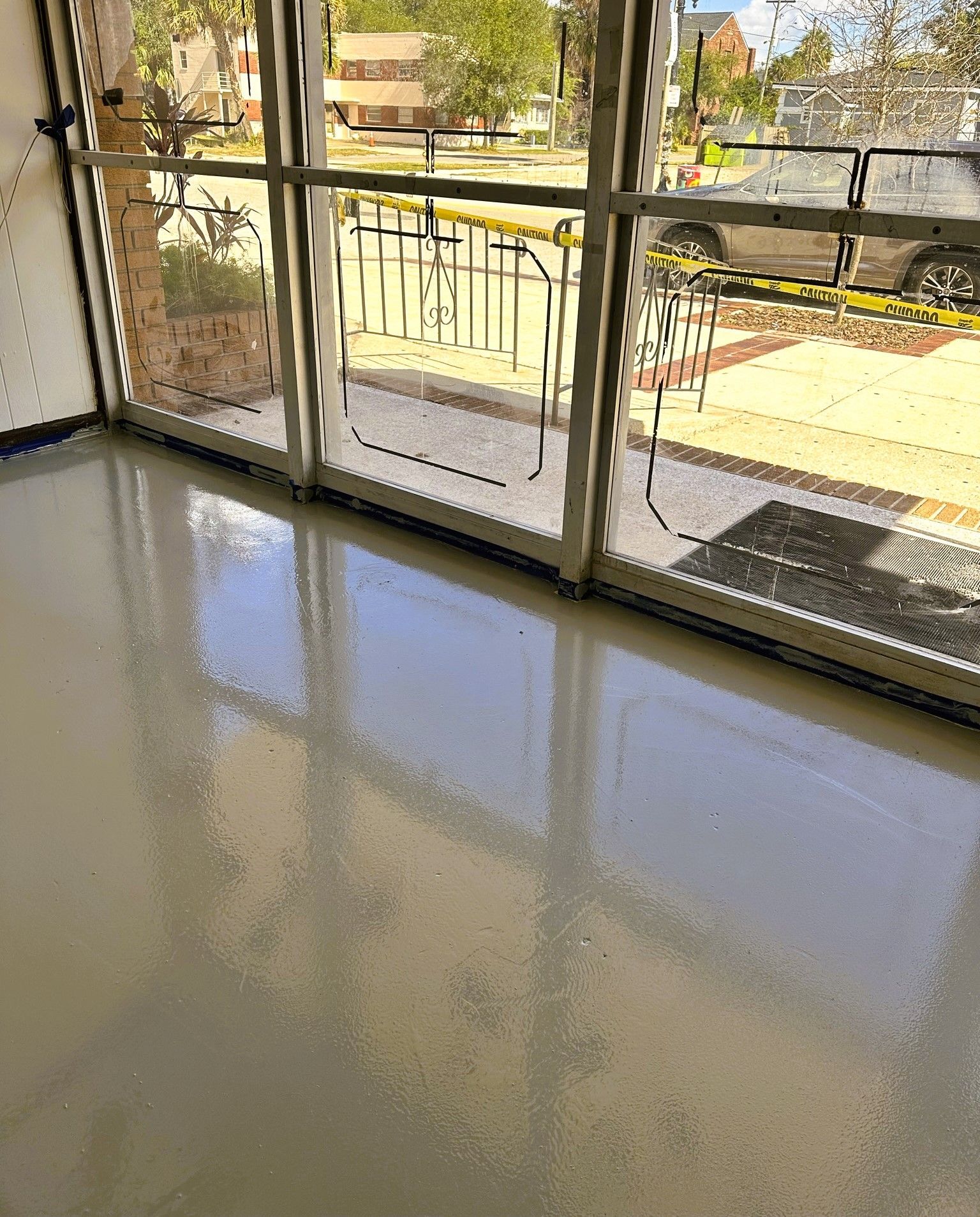 Sunlit empty room with glossy floor and large windows overlooking a patio and yard