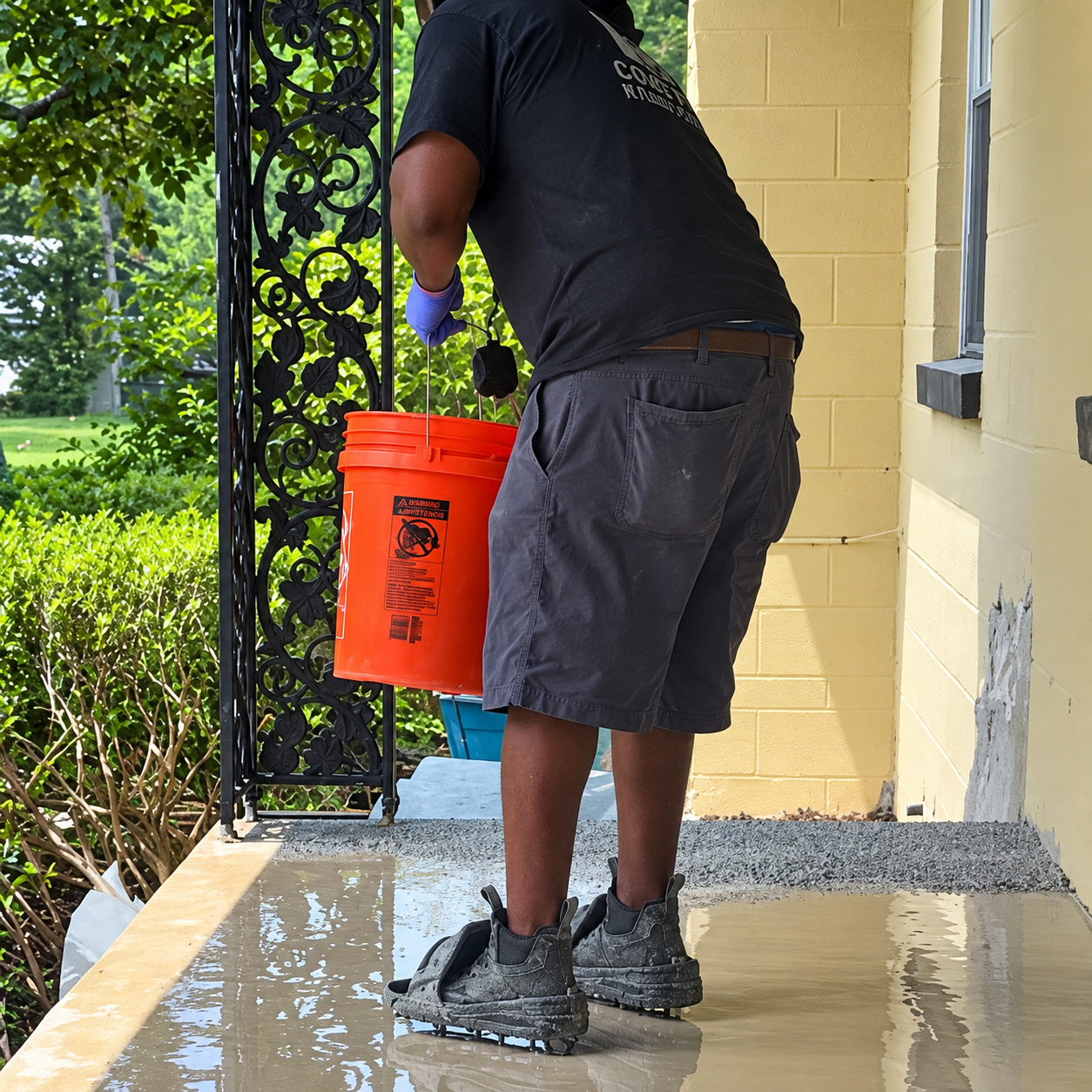 A man is holding an orange bucket and broadcasting vinyl flakes onto concrete porch
