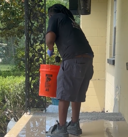 A man is standing on a porch holding an orange bucket
