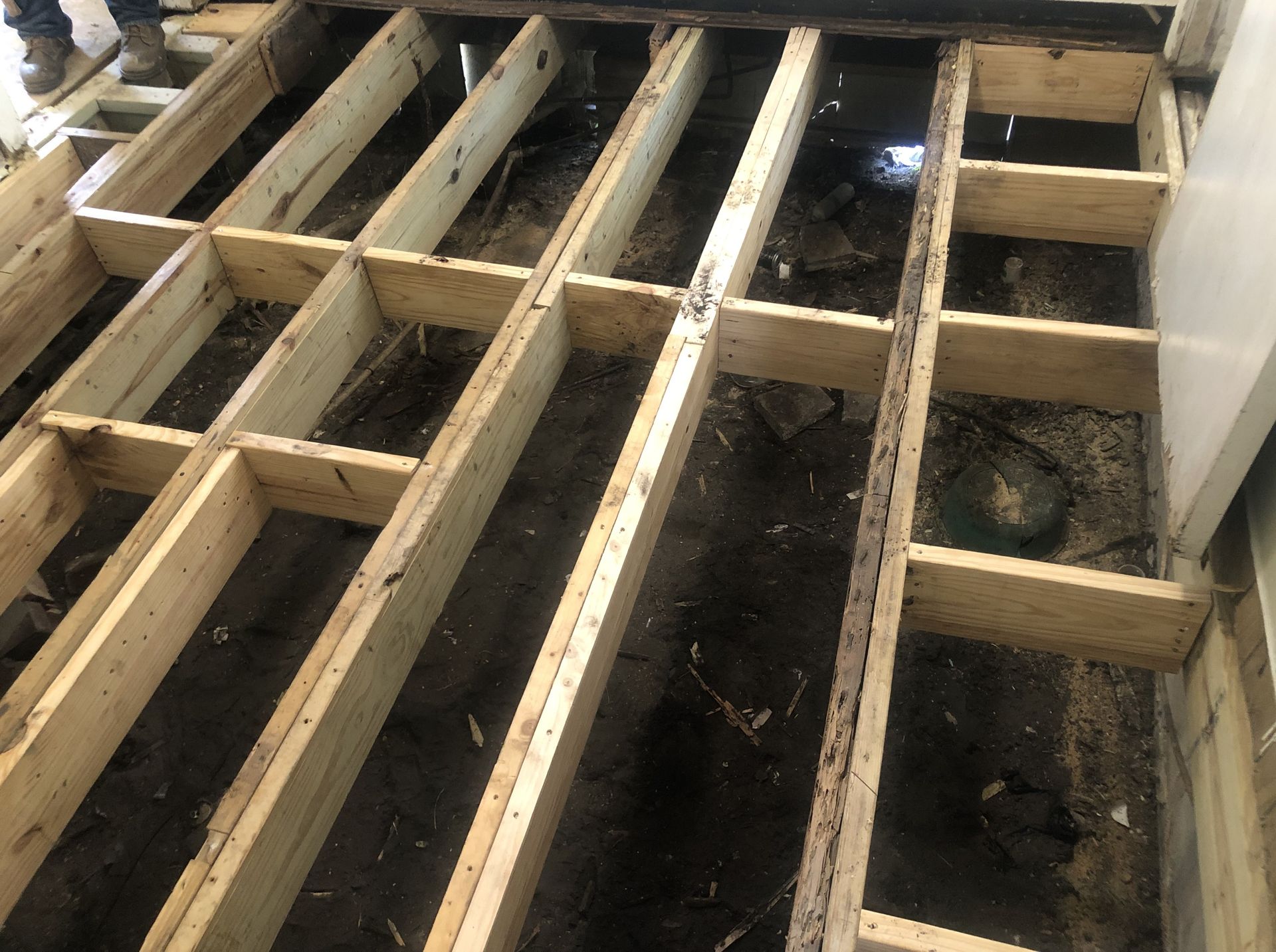 Exposed wooden floor joists over a dirt crawlspace with a few loose cables and debris.