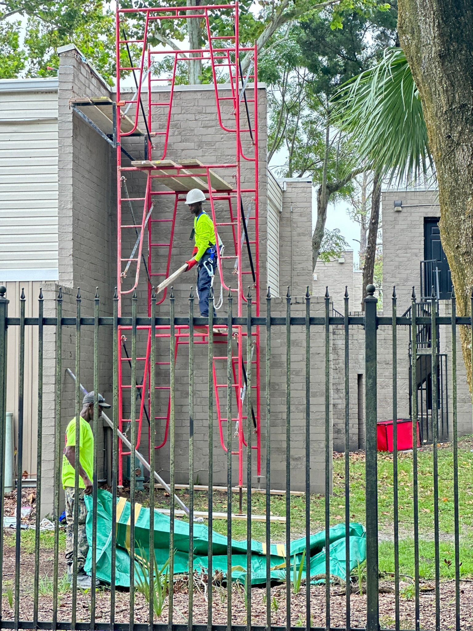 A construction worker is standing on a scaffolding next to a fence.