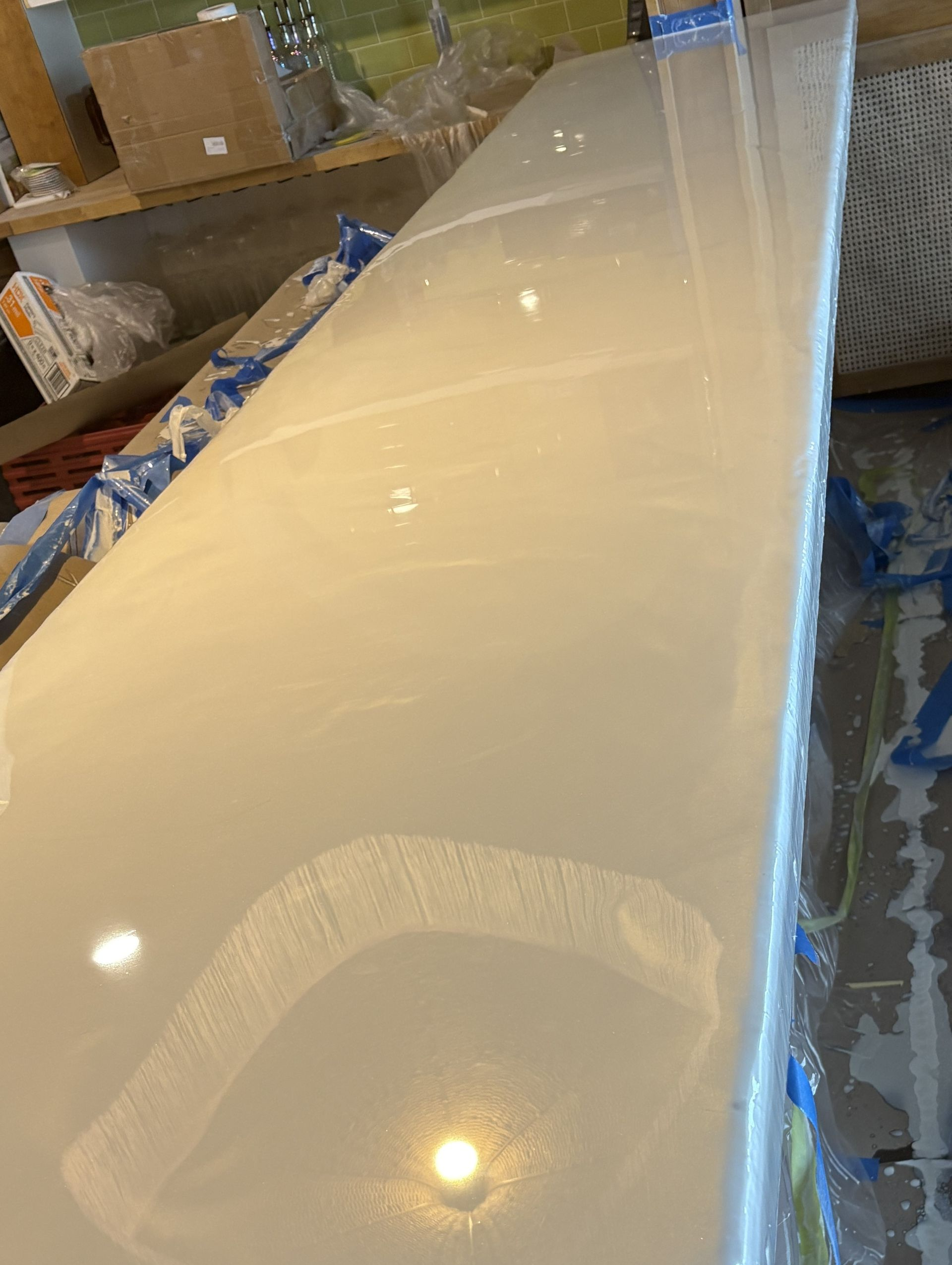 Glossy cream-colored epoxy countertop slab with blue tape along the edge in a warehouse
