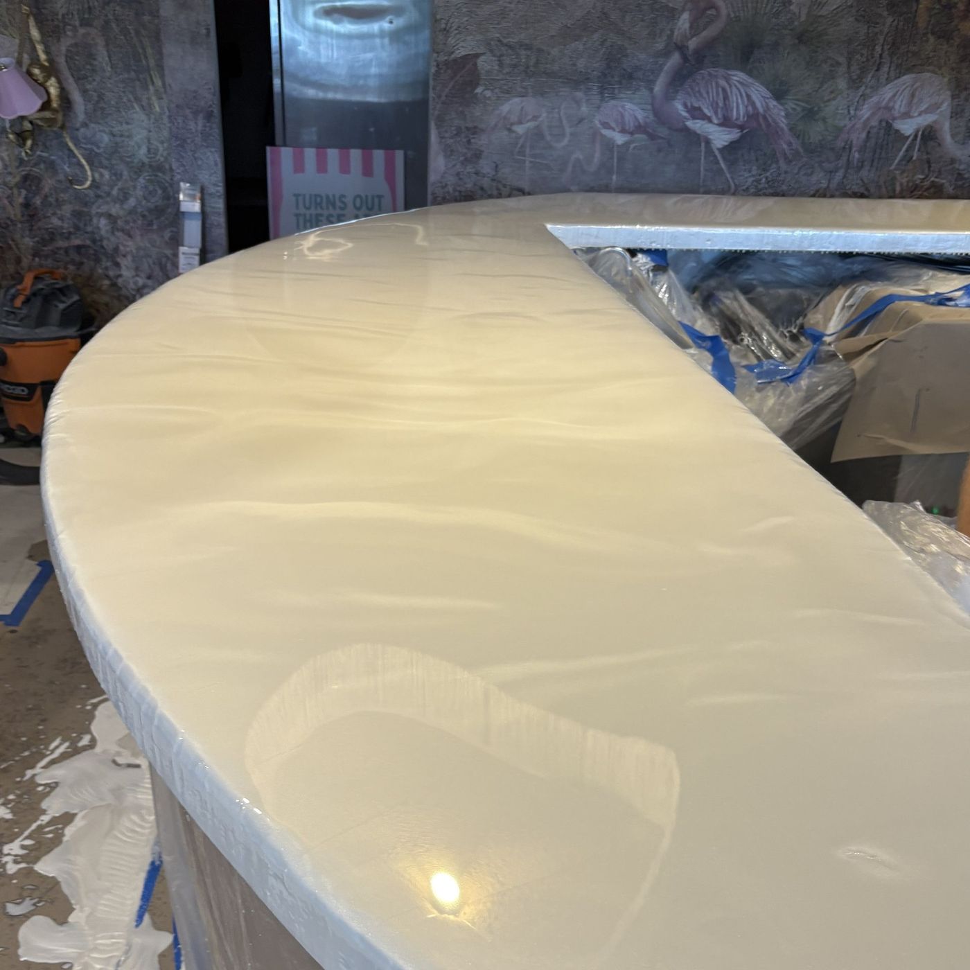 Glossy cream-colored curved countertop in a workshop, with protective tape and tools nearby