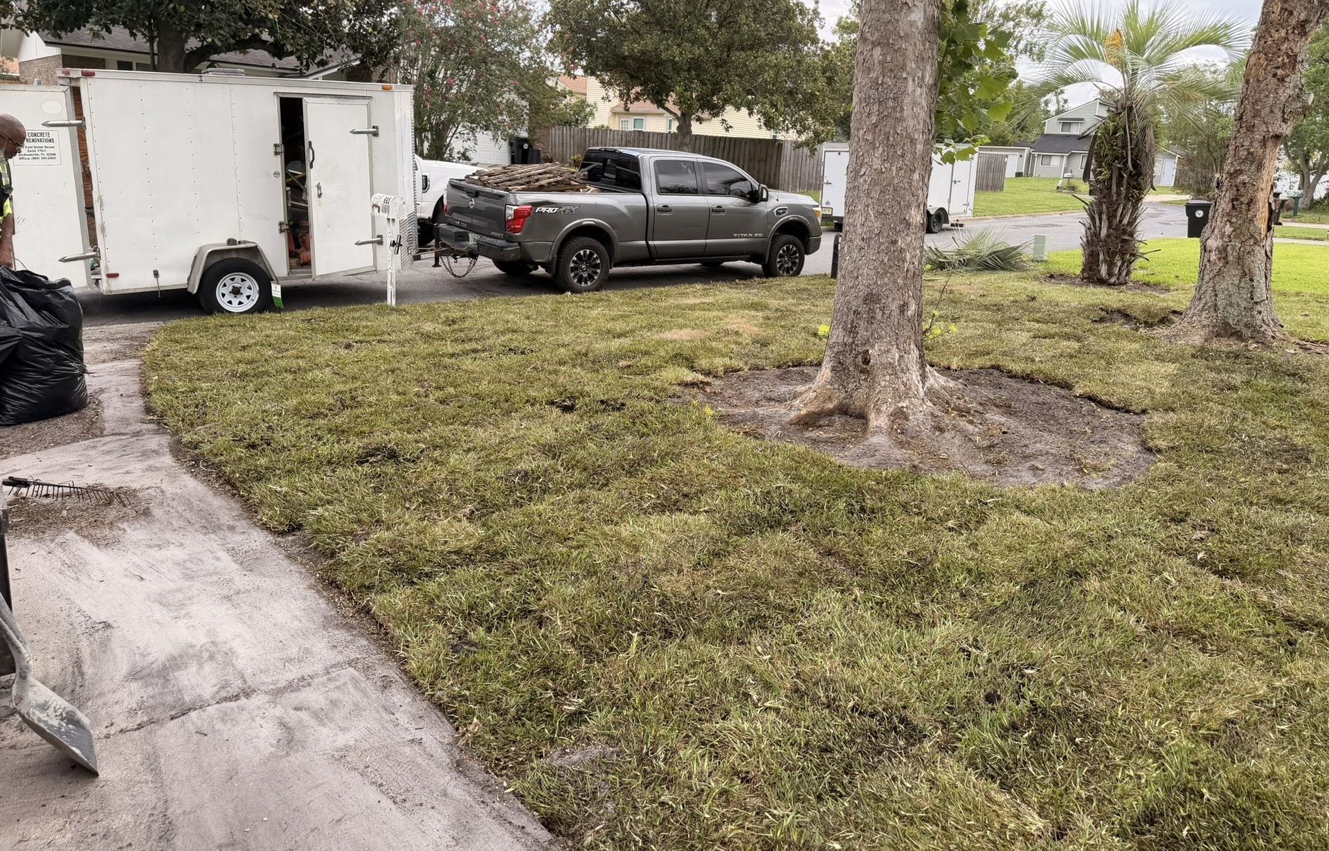 Rainy suburban driveway with a black pickup truck parked beside a white trailer and trees.