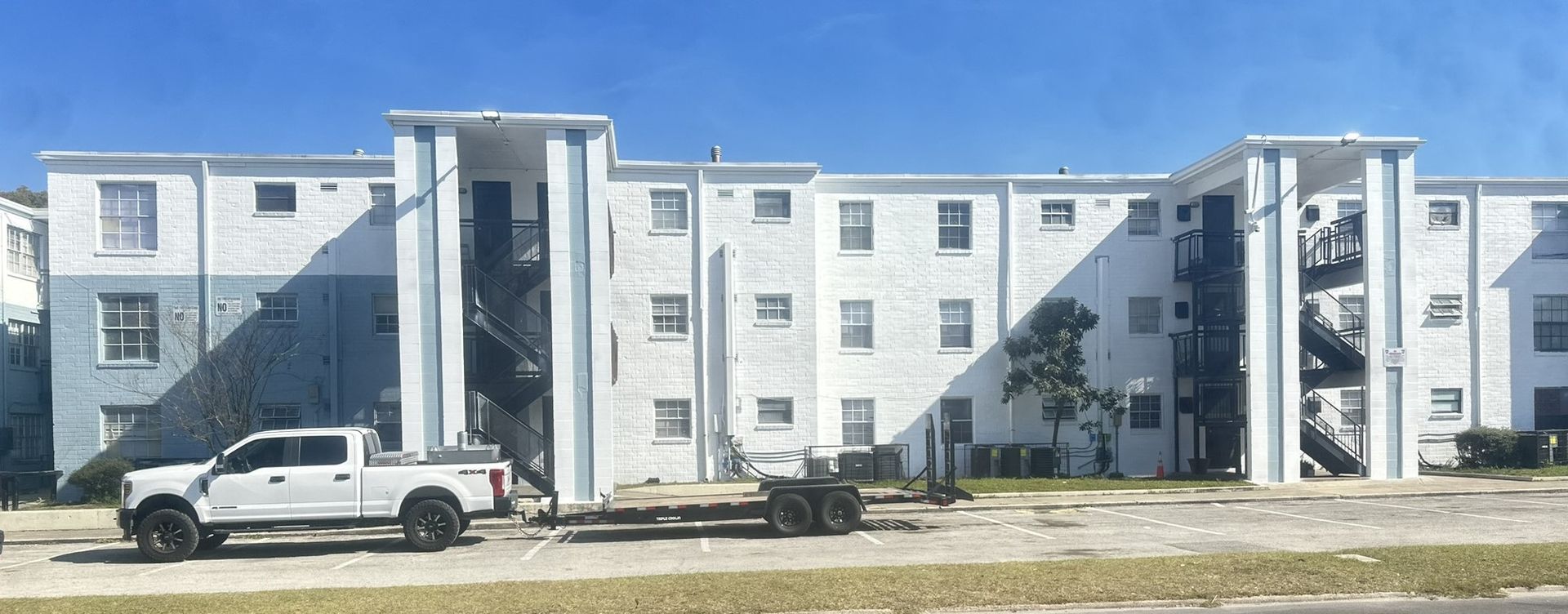 A white truck is parked in front of a large freshly painted white building.