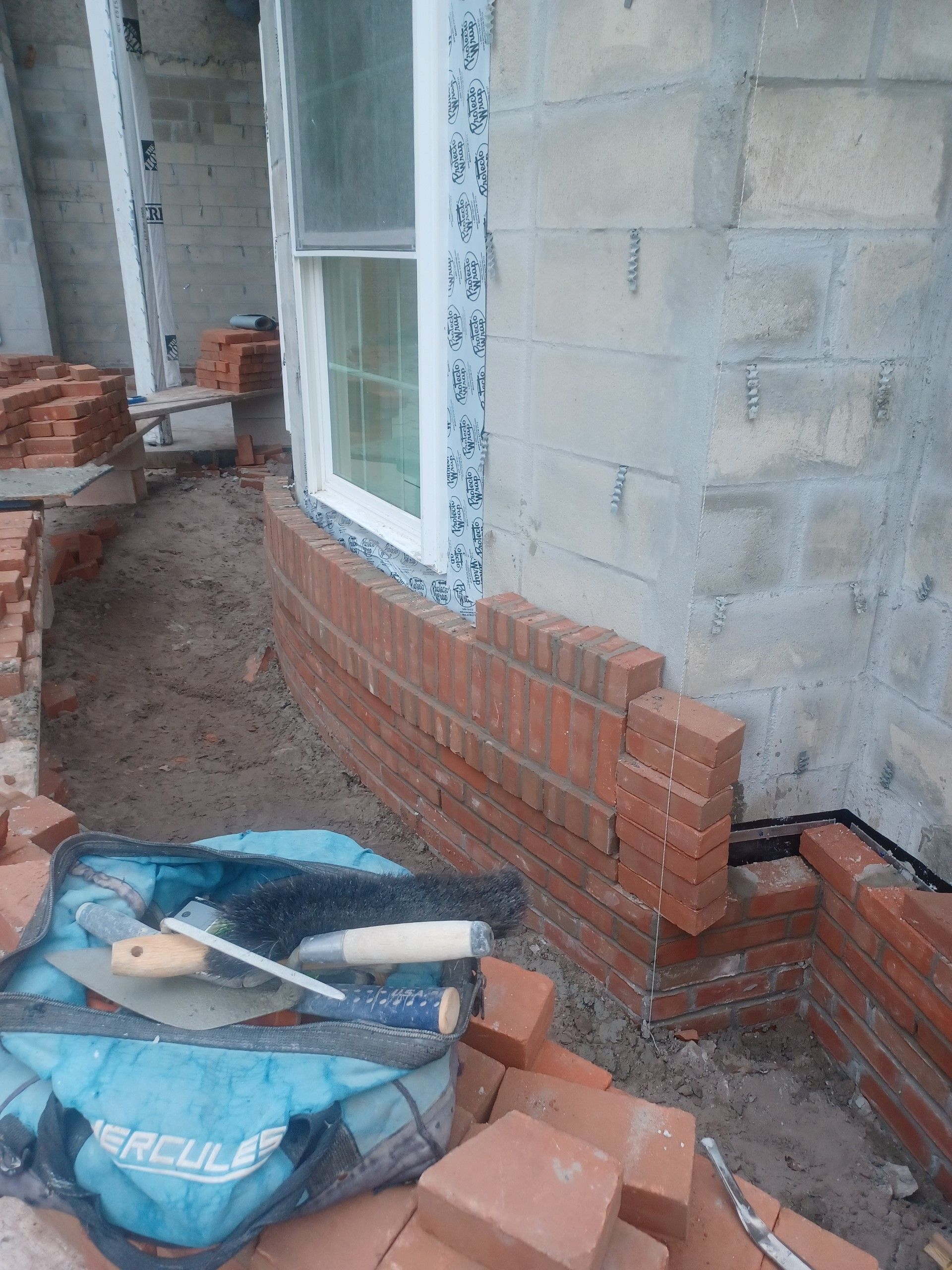A bag of tools is sitting on top of a pile of bricks next to a window.