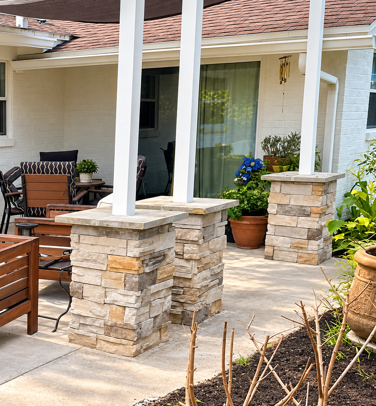 Stone porch columns and patio seating outside a house with potted plants and a sliding glass door
