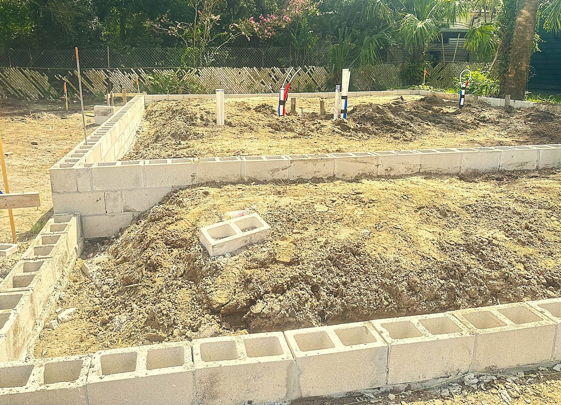 A small raised garden bed with dry soil, bordered by concrete blocks, in a sunny yard.