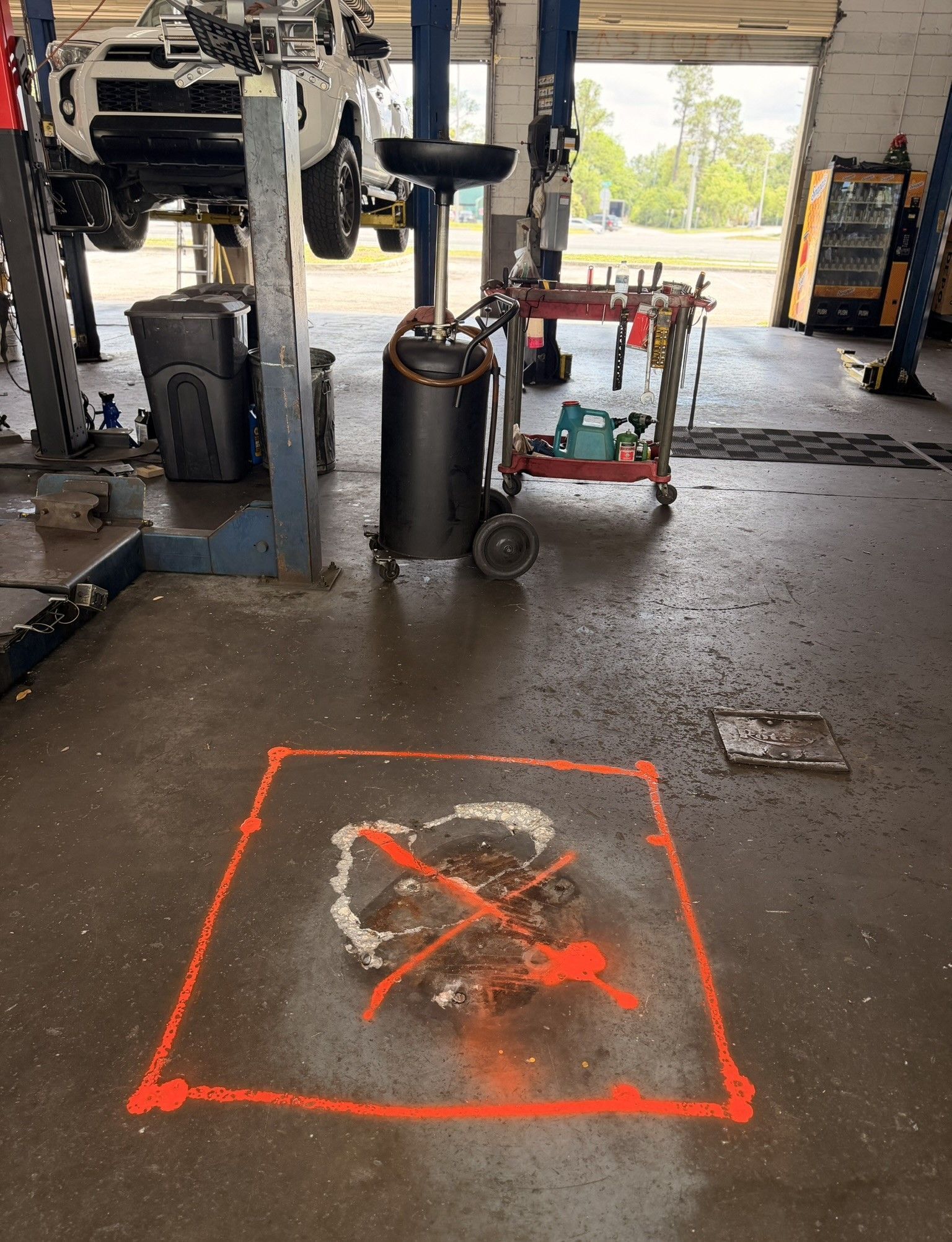 Orange taped square around a broken, wet floor area in an auto shop bay with equipment nearby